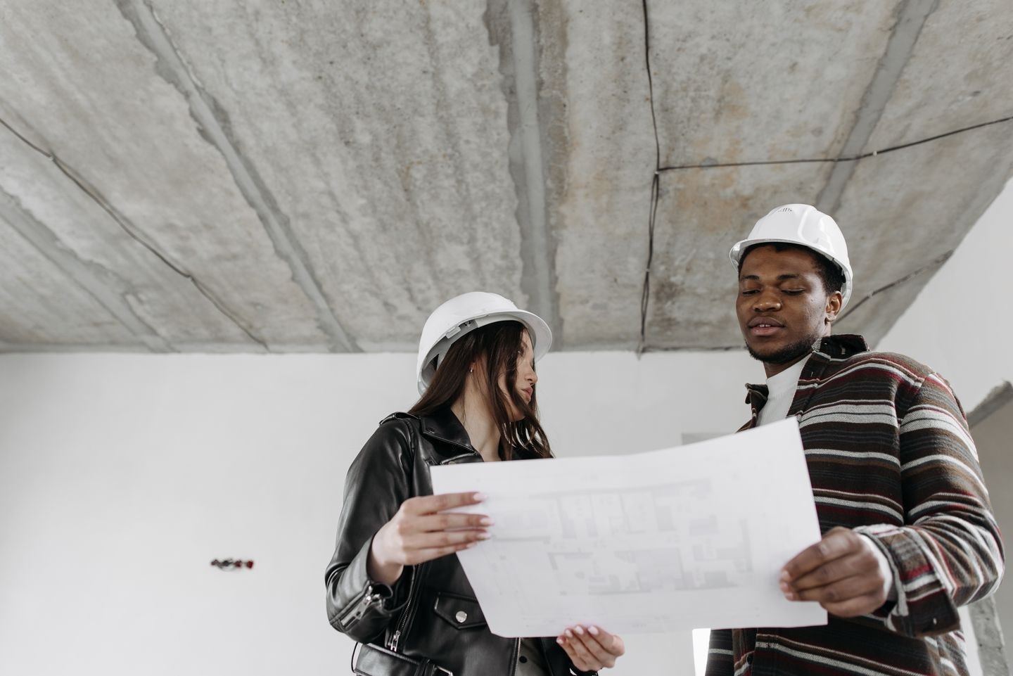 Two architects in hard hats examining blueprints in an unfinished building.